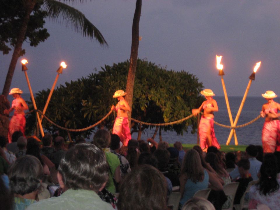 People watching hula dancers perform by torches near the ocean at dusk