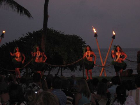 1991 Ford Bronco - A group of hula dancers perform on a stage illuminated by torches as the sun sets over the ocean.