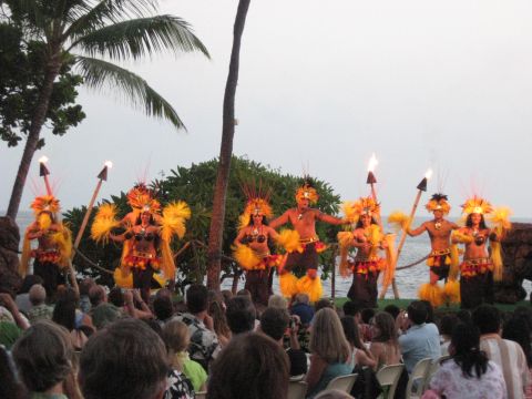 1991 Ford Bronco - A group of dancers in traditional Hawaiian costumes perform with torches on a beach, with palm trees and the ocean in the background.