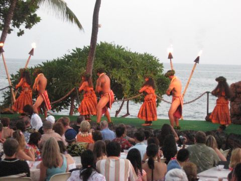 1991 Ford Bronco - A group of dancers perform a traditional hula dance on a stage overlooking the ocean, with an audience seated in front.