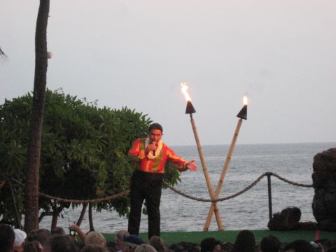 1991 Ford Bronco - A performer entertains an audience on a stage set against the ocean backdrop, illuminated by tiki torches.