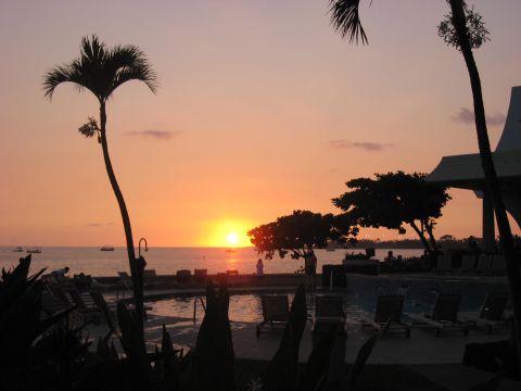 1991 Ford Bronco - A tranquil sunset scene unfolds over the ocean, with palm trees framing the view and lounge chairs near a pool.