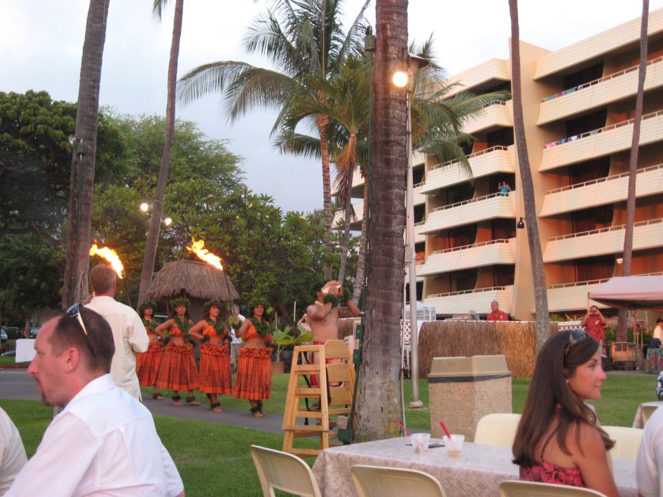 People watch a luau performance with fire dancers in front of a hotel building