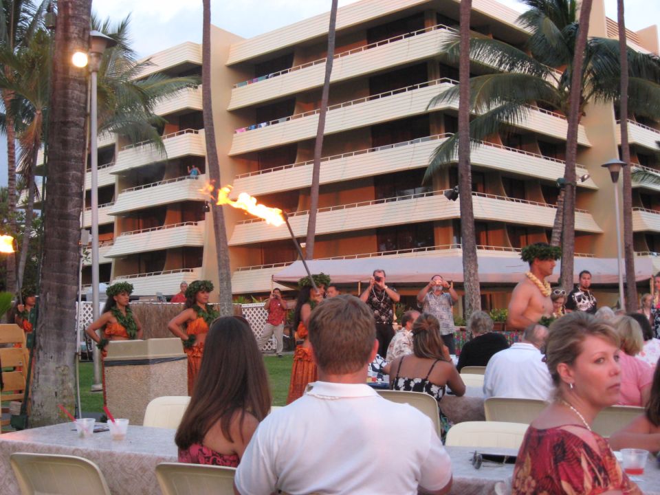People watch a fire dancer at a luau in front of a hotel with palm trees