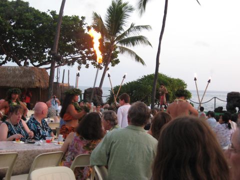 1991 Ford Bronco - An outdoor luau features fire dancers and performers on a stage near the ocean, with an audience seated at tables.