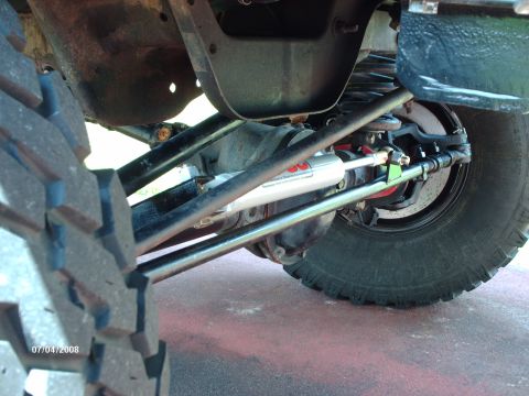 1982 Ford F-100 - A steering stabilizer shock is visible on the front axle of a vehicle, with a large tire in the foreground.