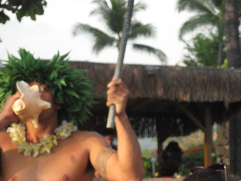1991 Ford Bronco - A man blows a conch shell while holding a staff, adorned with a lei and a green headdress.