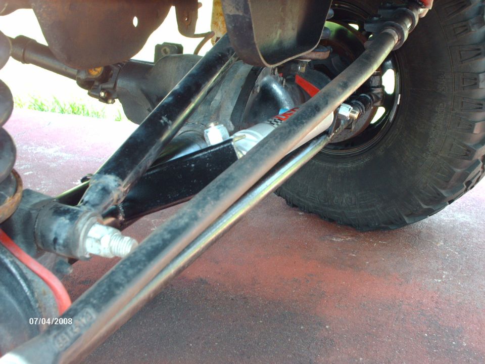Under-truck view of solid front axle, black radius arm, tie rod and steering stabilizer