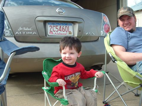 1979 Ford Bronco - A child sits in a green camping chair in front of a Nissan Altima sedan, with an adult to the right.