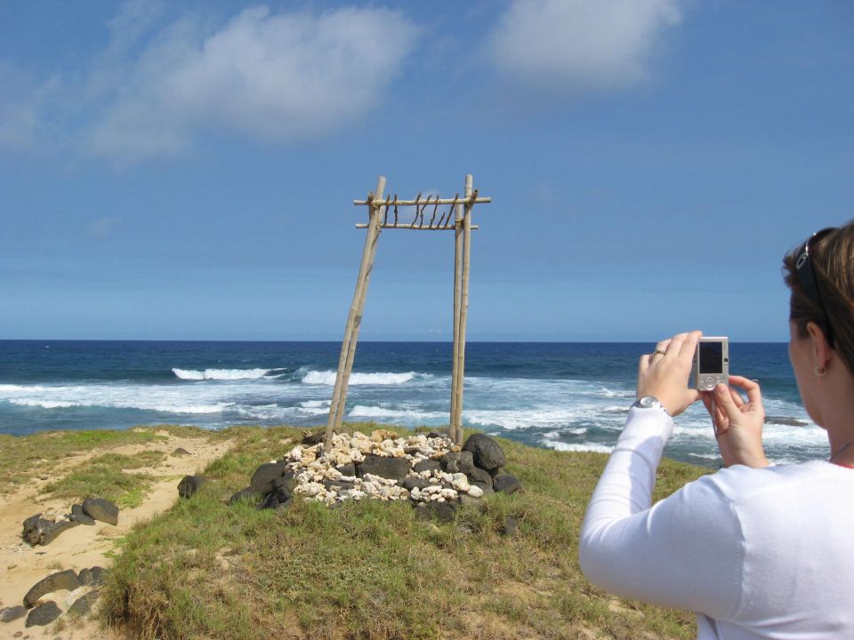 Woman photographs wooden structure on grassy cliff overlooking ocean waves
