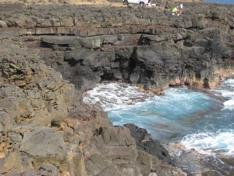 1991 Ford Bronco - A coastline features dark volcanic rocks and a small cove with churning blue water.
