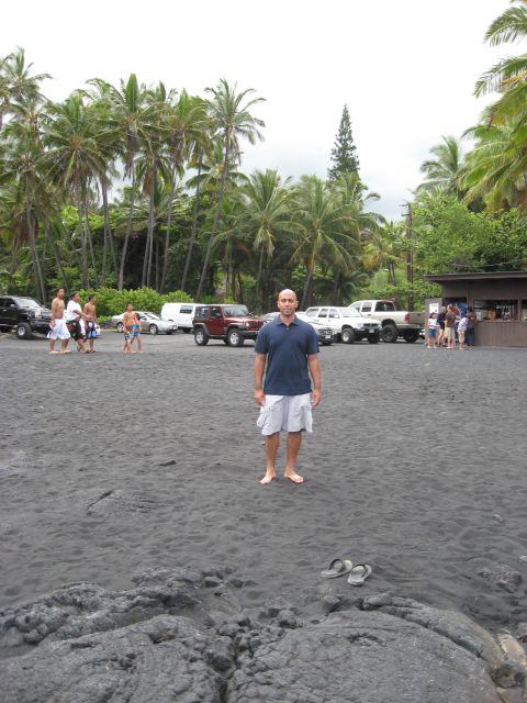 1991 Ford Bronco - A man stands on a black sand beach with parked vehicles and palm trees in the background.