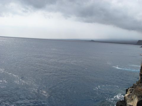 1991 Ford Bronco - A wide expanse of blue ocean meets a rocky coastline under a dramatic, cloudy sky.