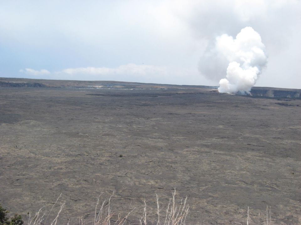 Volcanic landscape with a large plume of steam rising from a distant crater under a cloudy sky