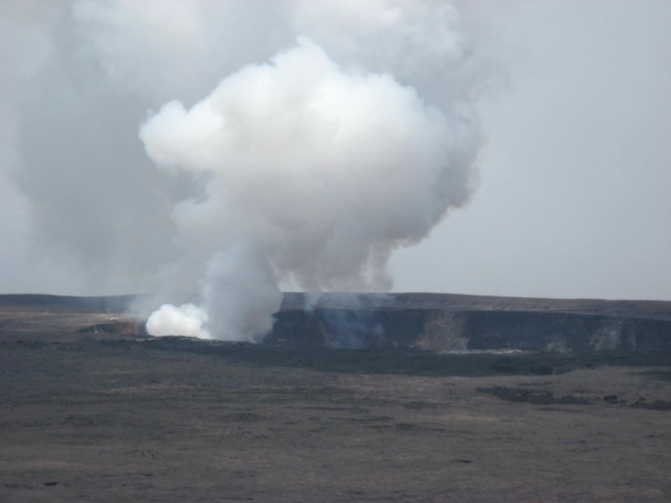 Volcanic crater emitting large smoke plumes under a hazy sky