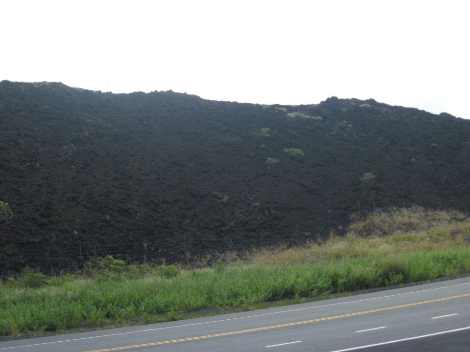 Volcanic rock slope with green grass and a road in the foreground