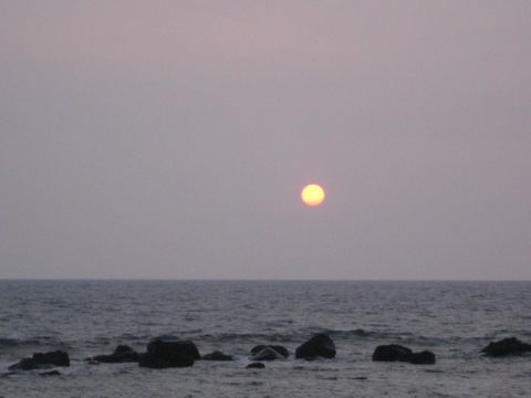 1991 Ford Bronco - The sun sets over the ocean, casting a warm glow on the water and silhouetting rocks near the shore.