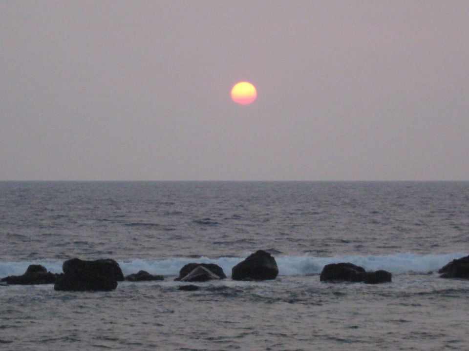 sun setting over the ocean with waves breaking on rocks
