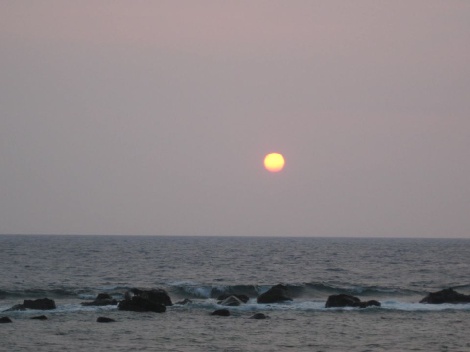 Sunset over the ocean with rocks in the foreground.