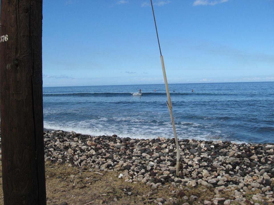 Wooden pole on a rocky beach with surfers in the ocean.
