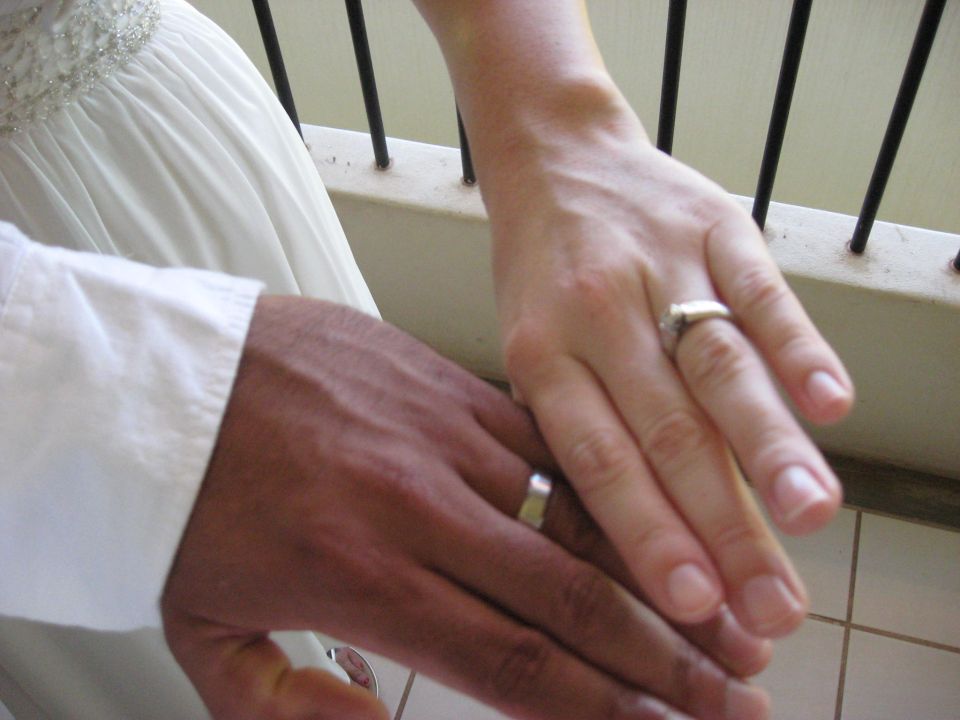 Two hands with wedding rings, one dark-skinned and one light-skinned