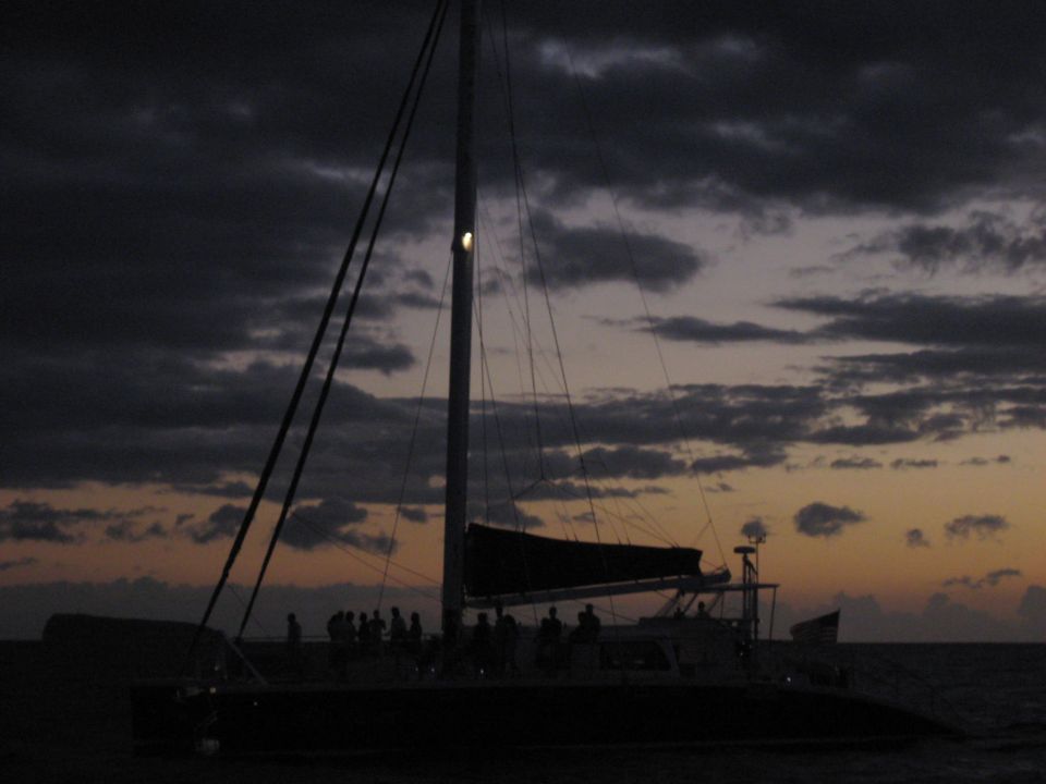 Silhouette of a catamaran sailing at sunset with dark clouds.