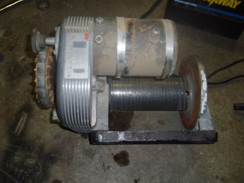 1980 Ford Bronco - A dusty, silver electric winch with a metal drum is mounted on a black metal base. The winch has a ribbed casing on the left side and a cyl…