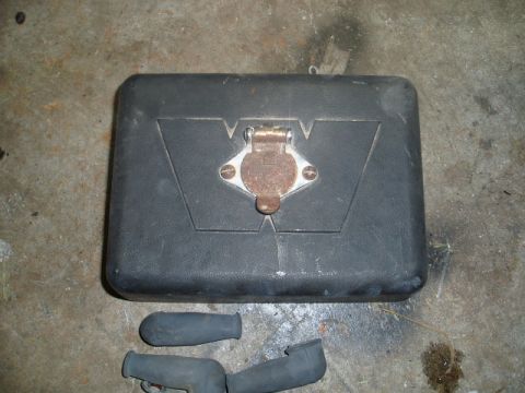 1980 Ford Bronco - A black rectangular case with a metal latch and a circular emblem is shown on a concrete floor. Two black rubber boot-like objects are visi…