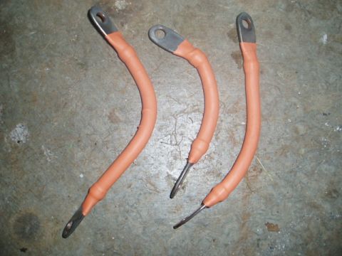 1980 Ford Bronco - Three copper battery cables with orange heat shrink tubing are laid out on a concrete floor. Each cable has a ring terminal on one end and…