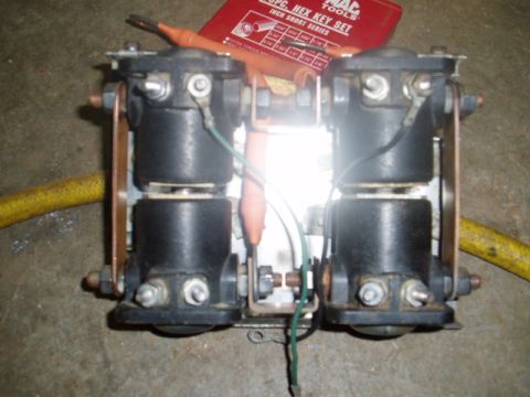 1980 Ford Bronco - A close-up view of two black solenoids mounted on a metal bracket, with copper connectors and wiring. A yellow hose is visible on the left…