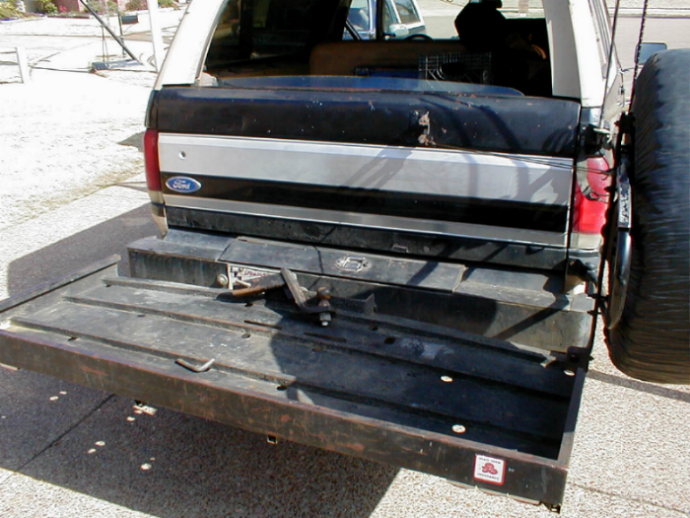 Open tailgate of a black-and-silver Ford SUV with rear-mounted spare and hitch