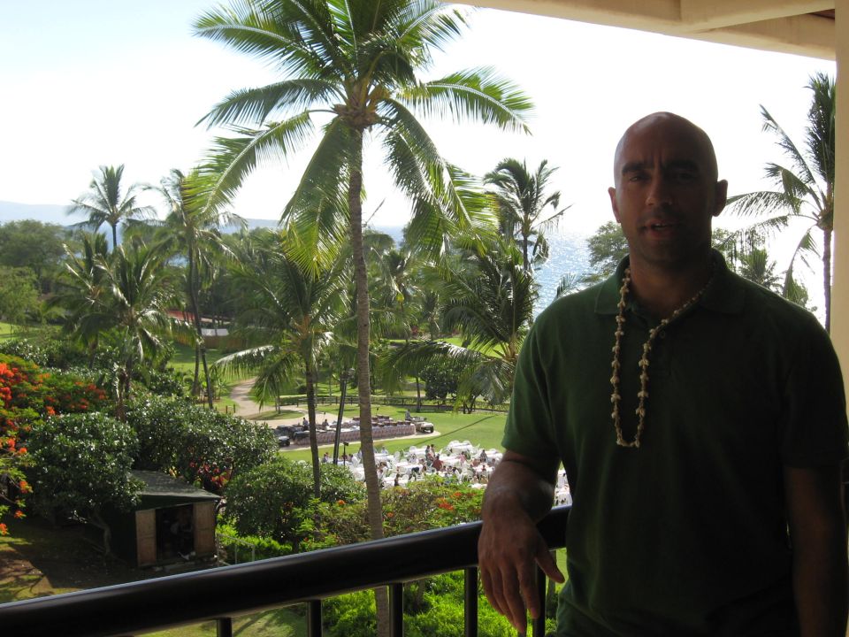 Man on a balcony with a tropical view of palm trees and the ocean.