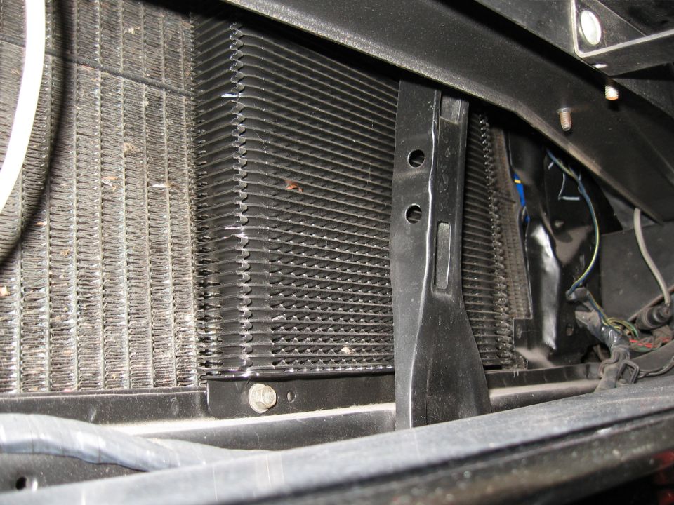 Close-up of vehicle radiator and transmission cooler fins with mounting hardware.