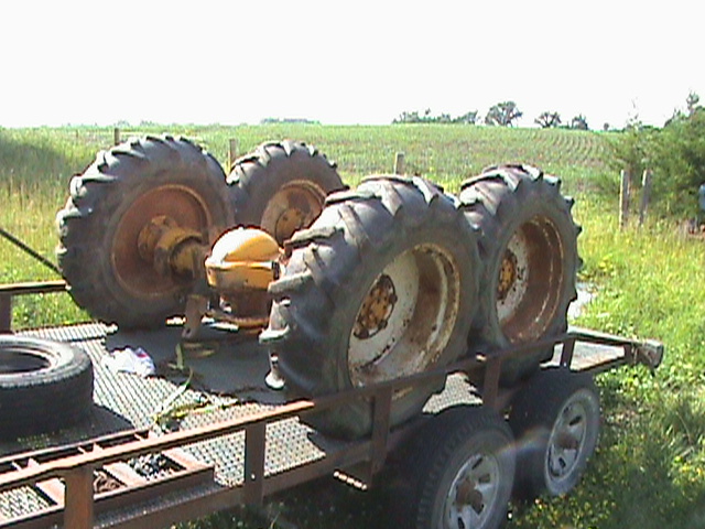 Trailer loaded with large tractor tires and a yellow component in a field.
