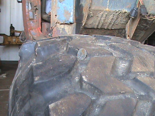 Close-up of a coin stuck in the tread of a large, worn vehicle tire.