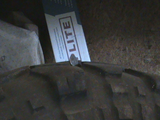 Coin stuck in tire tread with a cardboard box in the background.