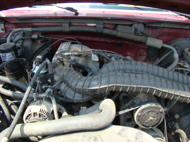 Engine bay of a red 1993 Ford Bronco, showing alternator, air intake, and belts.