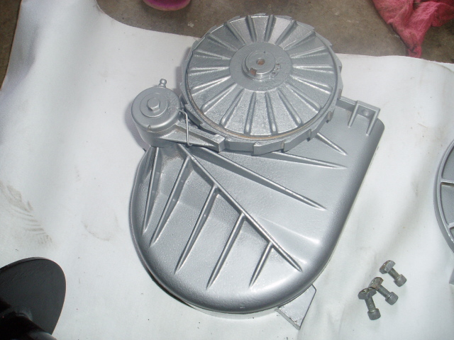 Silver painted automotive part with fins and a circular component, with bolts nearby.