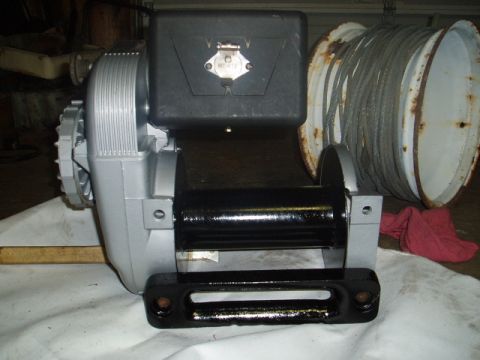 1980 Ford Bronco - A silver and black electric winch with a large spool of cable is shown on a white cloth. A black tow hook is mounted to the front of the wi…