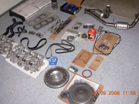 1988 Ford F-150 — Engine parts including blocks, gaskets, belts, injectors, catalytic converter, and clutch on a garage floor.