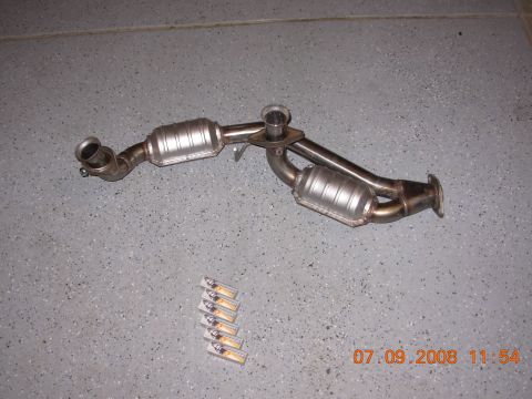 1988 Ford F-150 — Dual catalytic converter exhaust system on a gray speckled floor with six small rectangular items below.