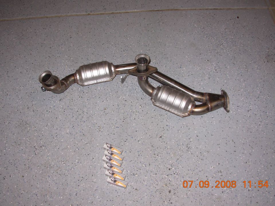 Dual catalytic converter exhaust system on a gray speckled floor with six small rectangular items below.