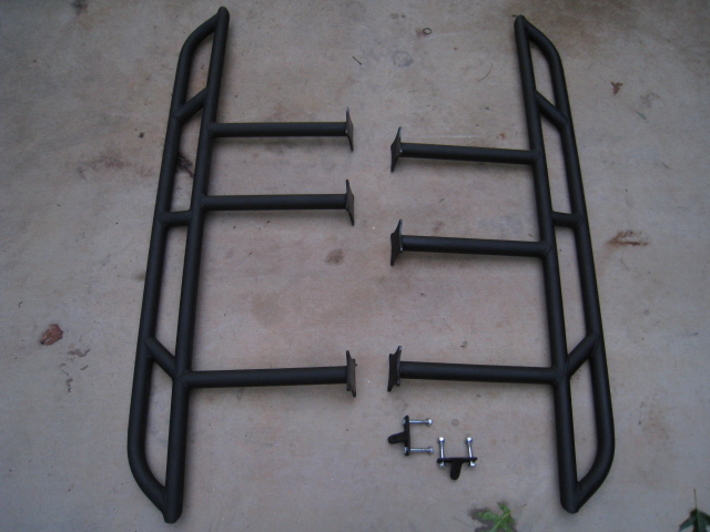 Pair of black tubular side steps with mounting feet laid on concrete