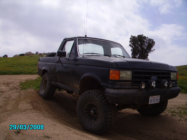 Black lifted Ford Bronco with KC spotlights on a dirt track.