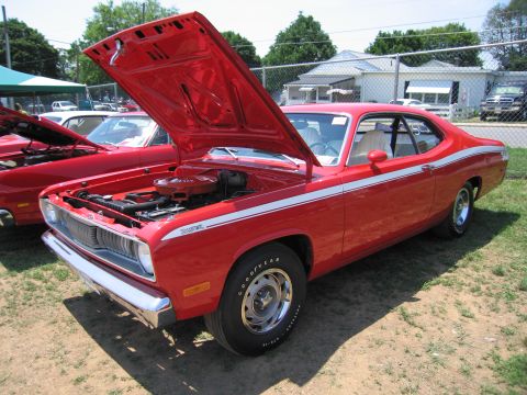 2001 Ford Crown Victoria - A red 1973 Plymouth Duster 340 is displayed with its hood open, revealing the engine bay. White racing stripes adorn its sides.