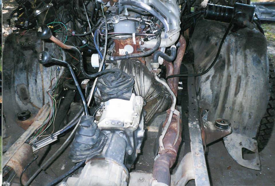 Engine compartment with engine and transmission visible, fenders removed, wiring exposed