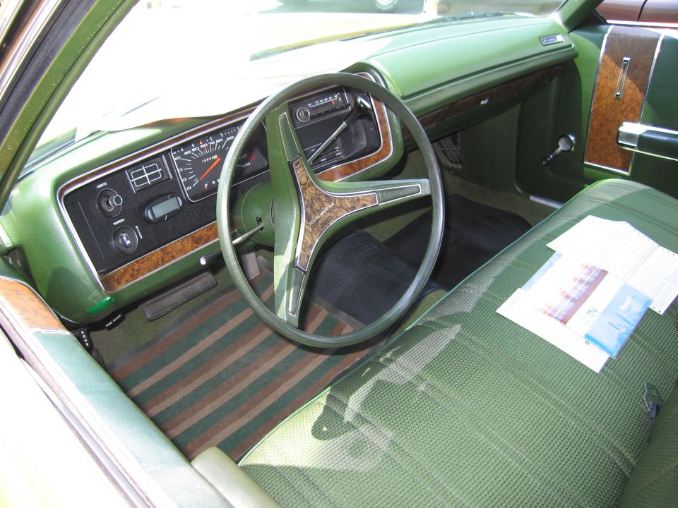 Green interior of a car with a wood-grain steering wheel and dashboard trim. Striped floor mats are visible