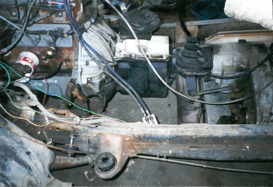 Chassis and transmission area with cables, reservoir, and rusty frame crossmember