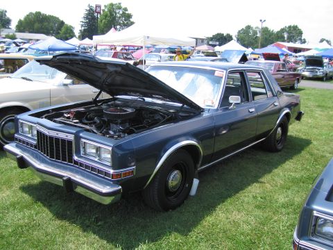 2001 Ford Crown Victoria - A dark blue sedan with its hood open, revealing the engine, sits on a grassy field at an outdoor event.