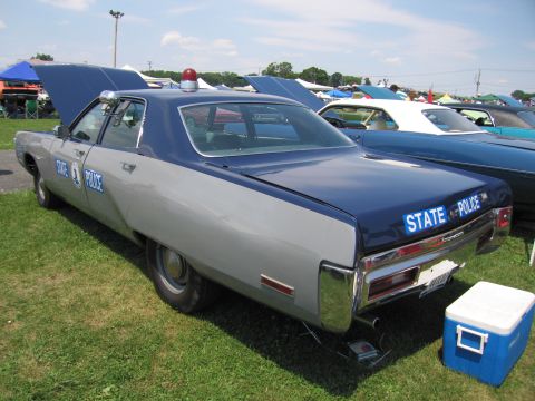 2001 Ford Crown Victoria - A vintage two-tone police car with "STATE POLICE" markings is parked on grass next to other vehicles.